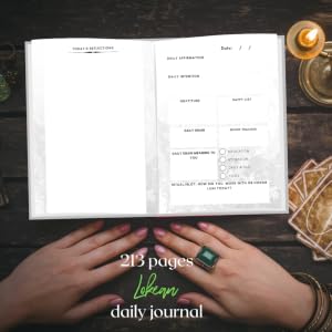 An open daily journal with blank and filled-in pages, shown on a dark wooden surface with hands holding the bottom edge. A candle, ring, and geometric decor are visible around it.